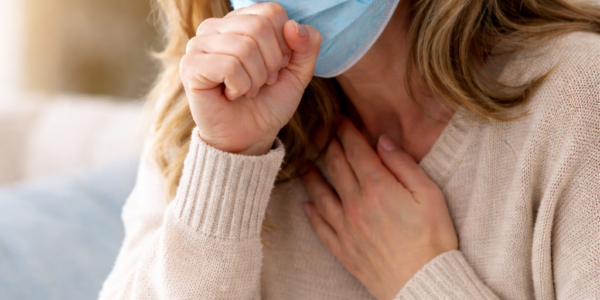 40 year old woman with blonde hair coughing into a blue surgical mask